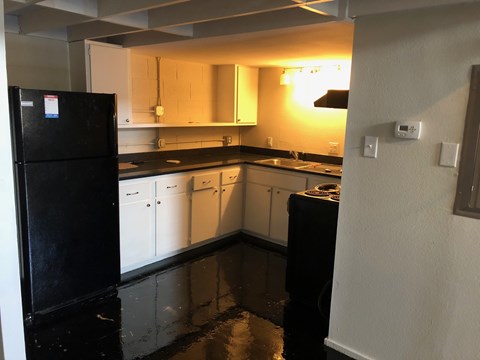 A black refrigerator sits in a kitchen with white cabinets.